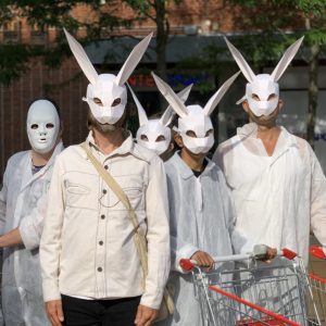 Fem skådespelare i kaninmask tittar rakt in i kameran, en håller i en kundvagn.